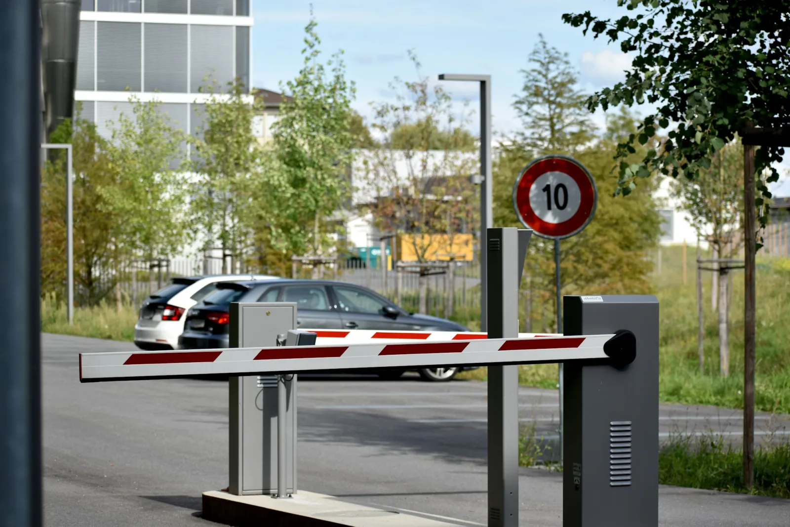 Hız sınırı levhası bulunan bir otopark girişinde kırmızı-beyaz bariyer kolu ve yaklaşan araç